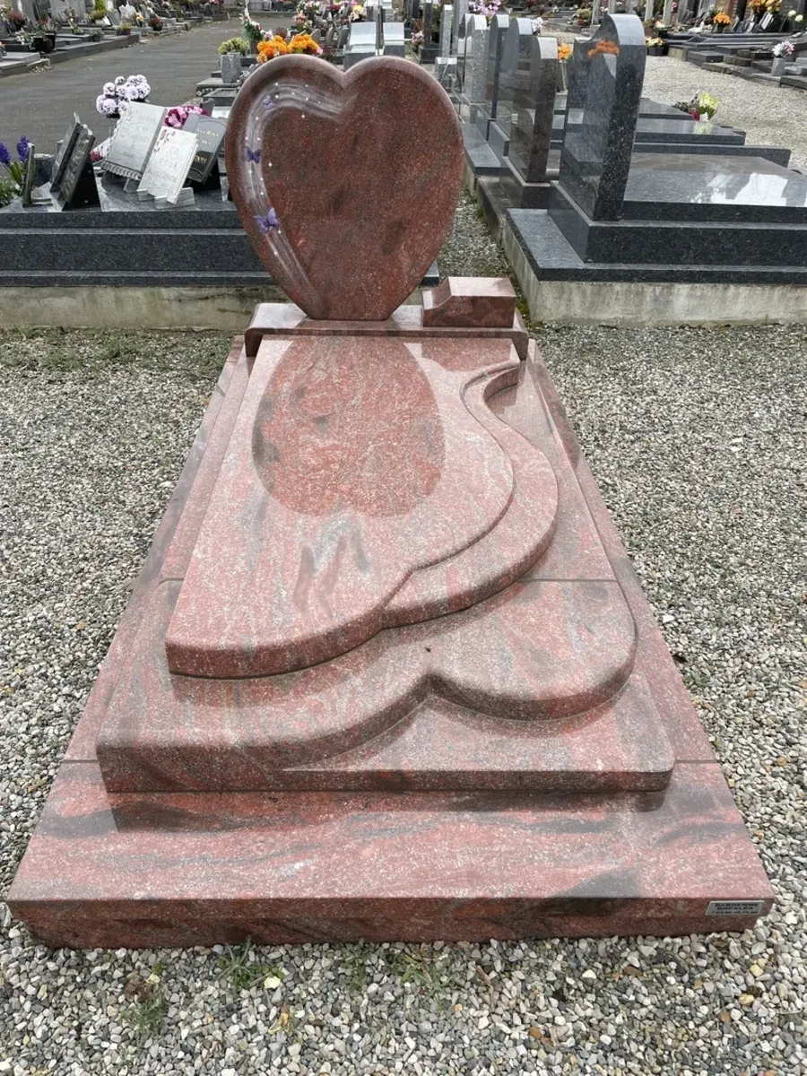 Pierre tombale en granit rouge en forme de cœur avec gravure et fleurs.