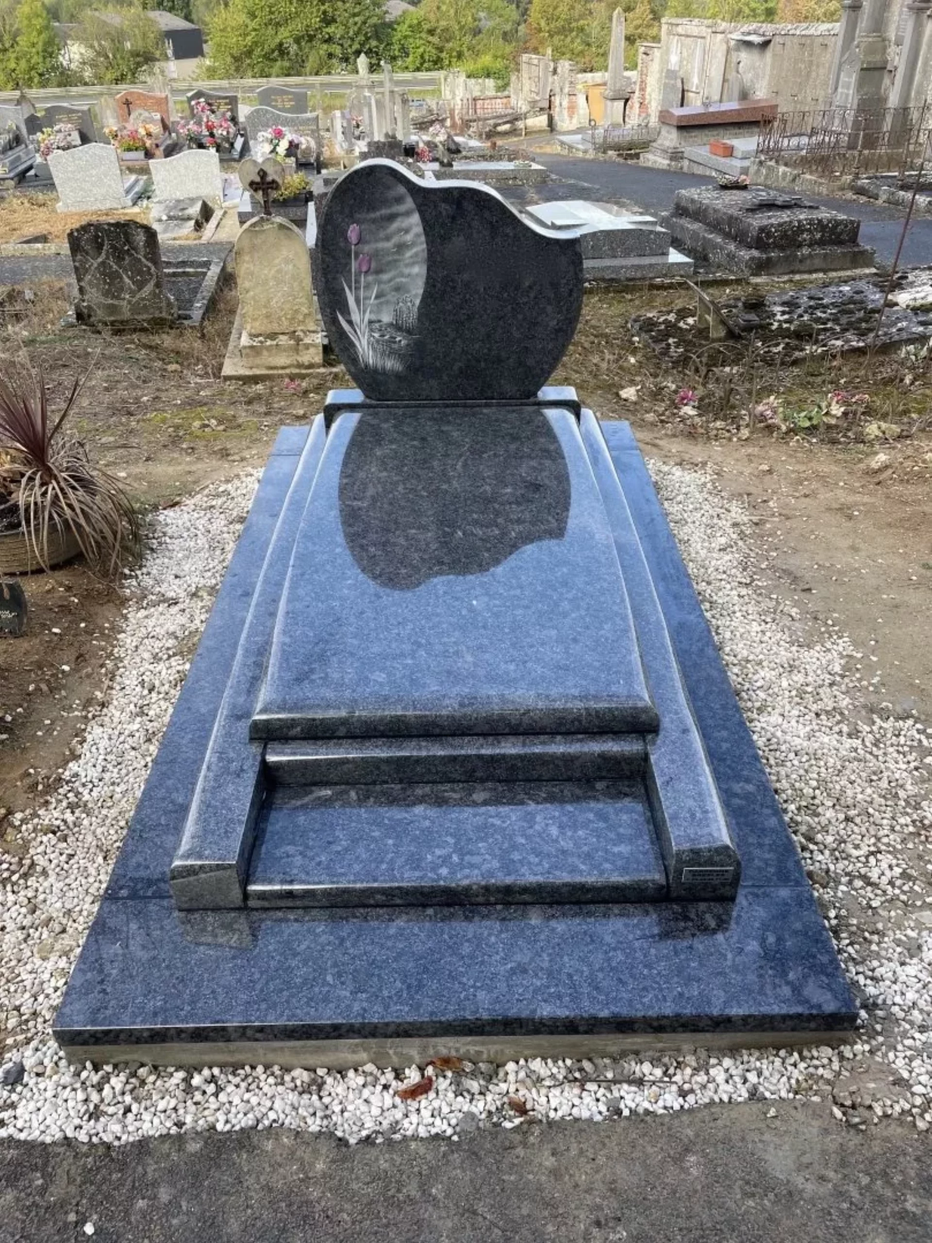Monument funéraire en granit bleu poli avec stèle en cœur et gravure florale.