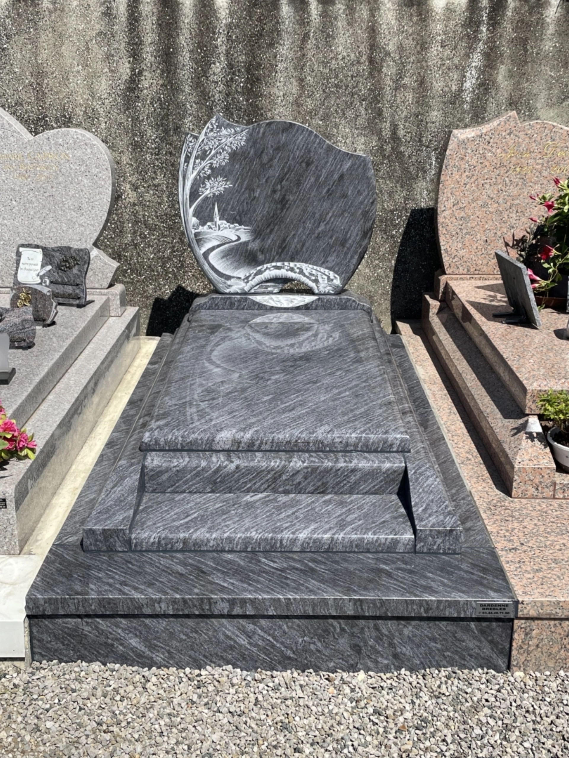 Tombe en granit gris veiné avec stèle décorée d'une scène de paysage.