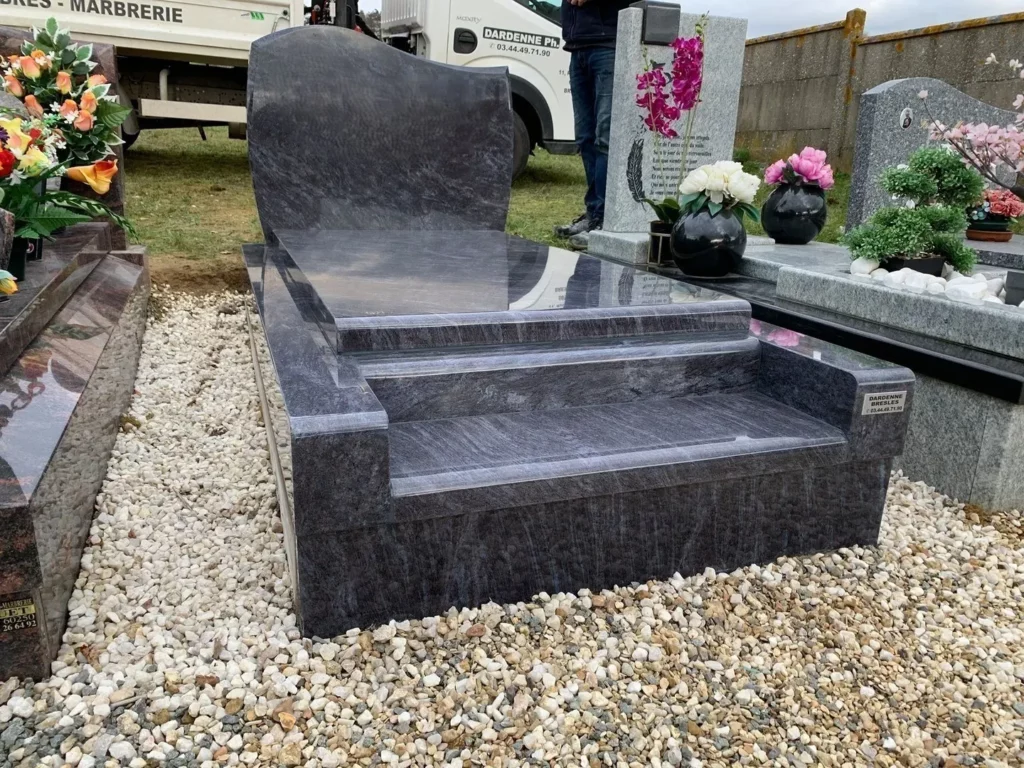 Monument funéraire en granit bleu posé au cimetière avec fleurs.
