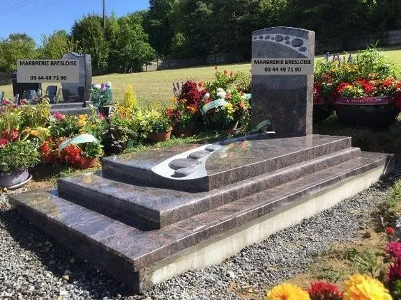 Tombe en granit rose avec aménagement paysager et fleurs au cimetière.