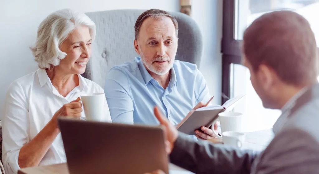 Couple de seniors souriant discutant avec un conseiller financier lors d'une réunion.